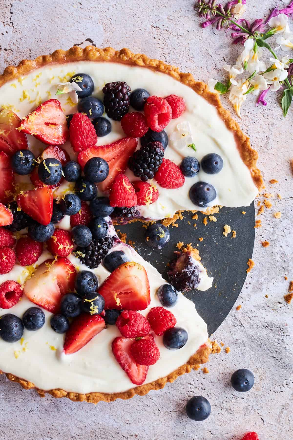 Overhead view of a cheesecake fruit tart with a slice missing.