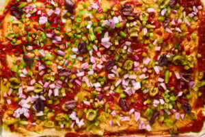Raw dinner rolls topped with pizza sauce, peppers, onions, and olives.