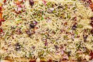 Raw dinner rolls topped with pizza sauce, chopped veggies, olives, and cheese.
