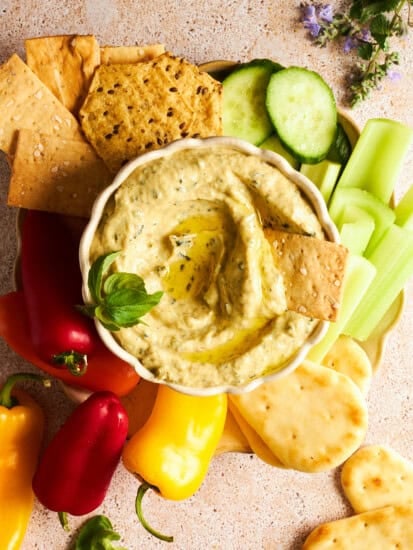 A bowl of zucchini dip with cucumbers, celery, pita, mini bell peppers, and crackers.