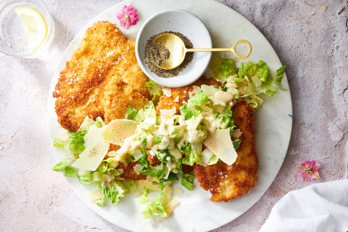 A plate of chicken Milanese topped with Caesar salad.