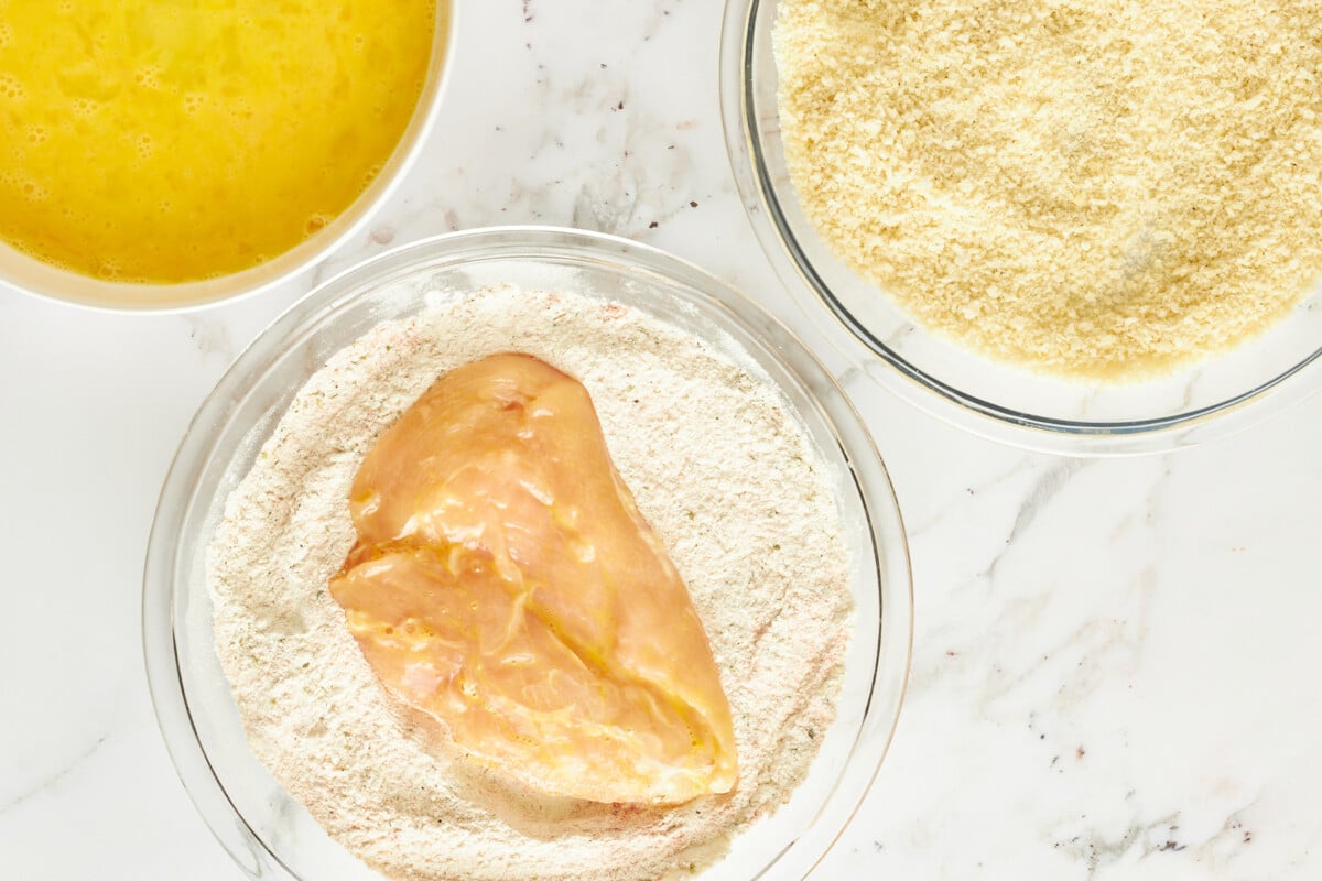 Raw chicken being dredged in flour.