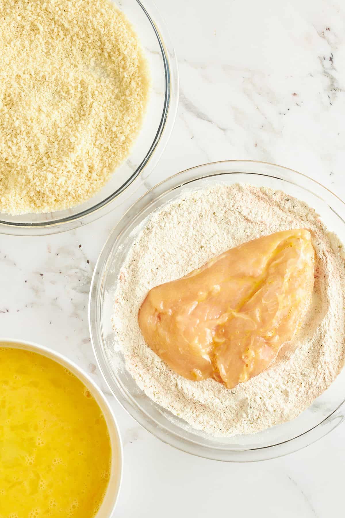 Raw chicken coated in egg in a bowl of flour. 