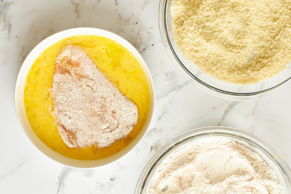 Floured chicken in a bowl of egg wash.