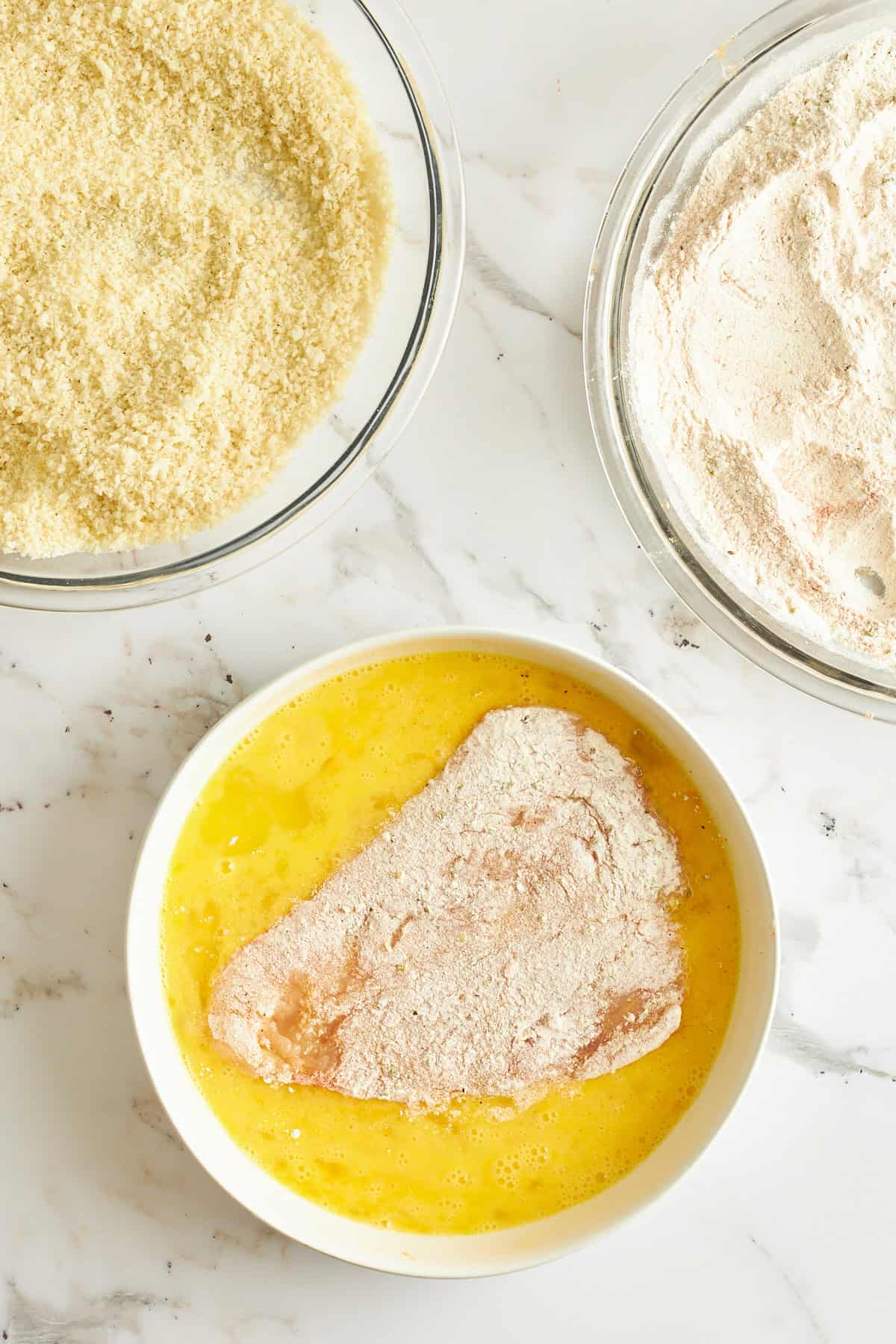 Raw breaded chicken in a bowl of egg wash. 