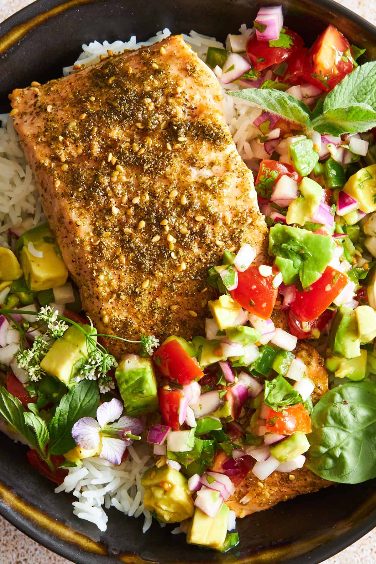Close up view of a bowl of rice with za'atar baked salmon and avocado salsa.