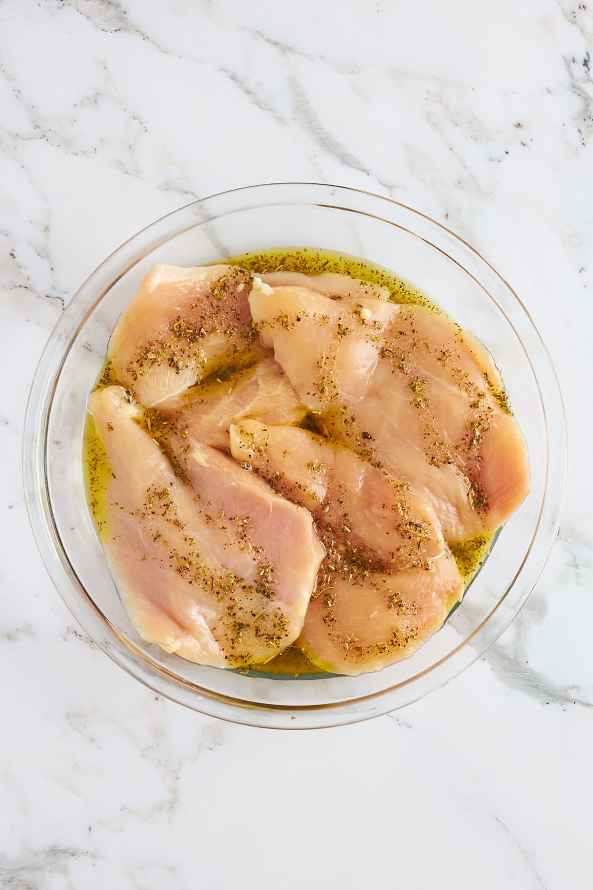 A bowl of chicken breasts in an olive oil marinade.