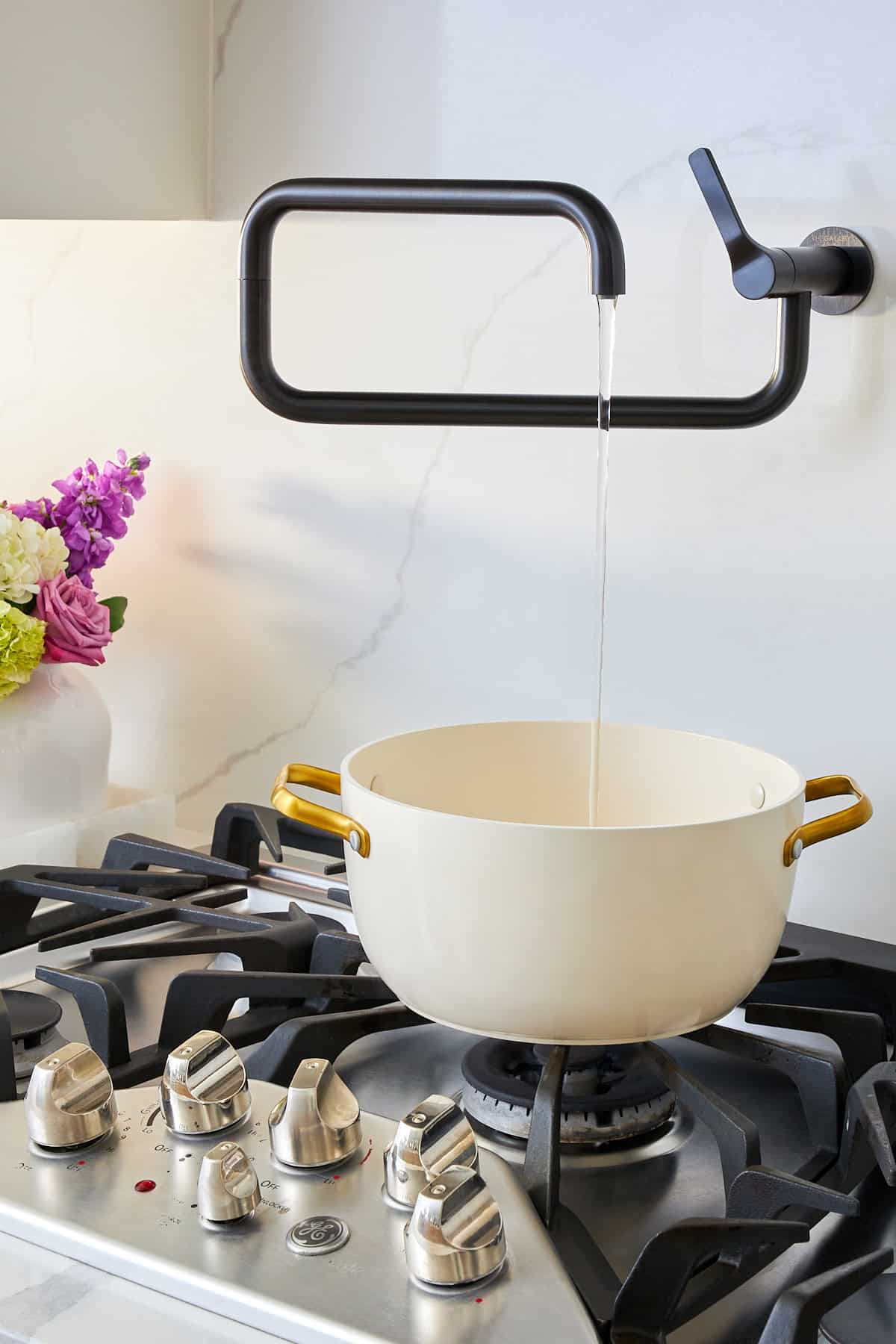 A water spout over a stove pouring water into a pot. 