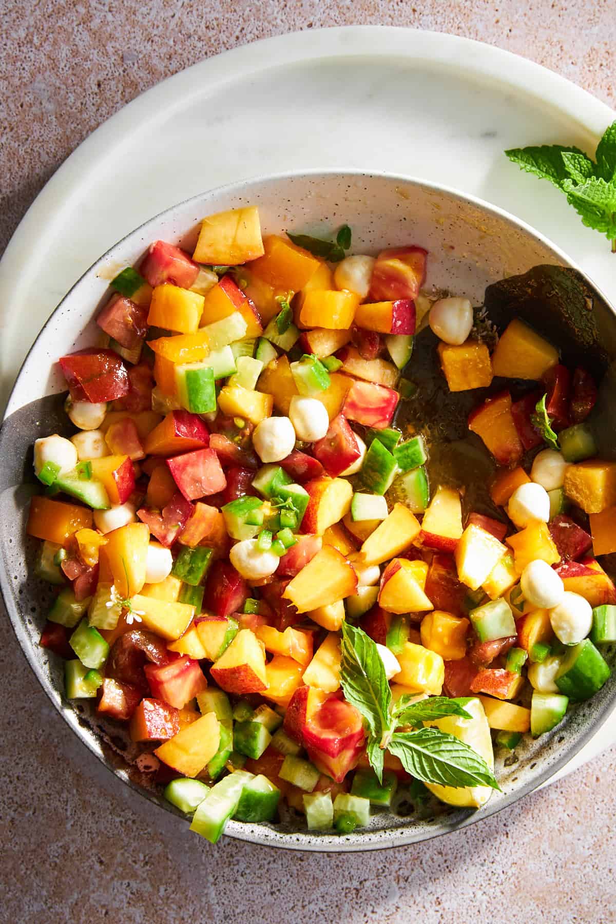 A bowl of peach salad with mozzarella pearls.