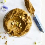 Overhead image of a jar of pistachio butter with a knife on the side.