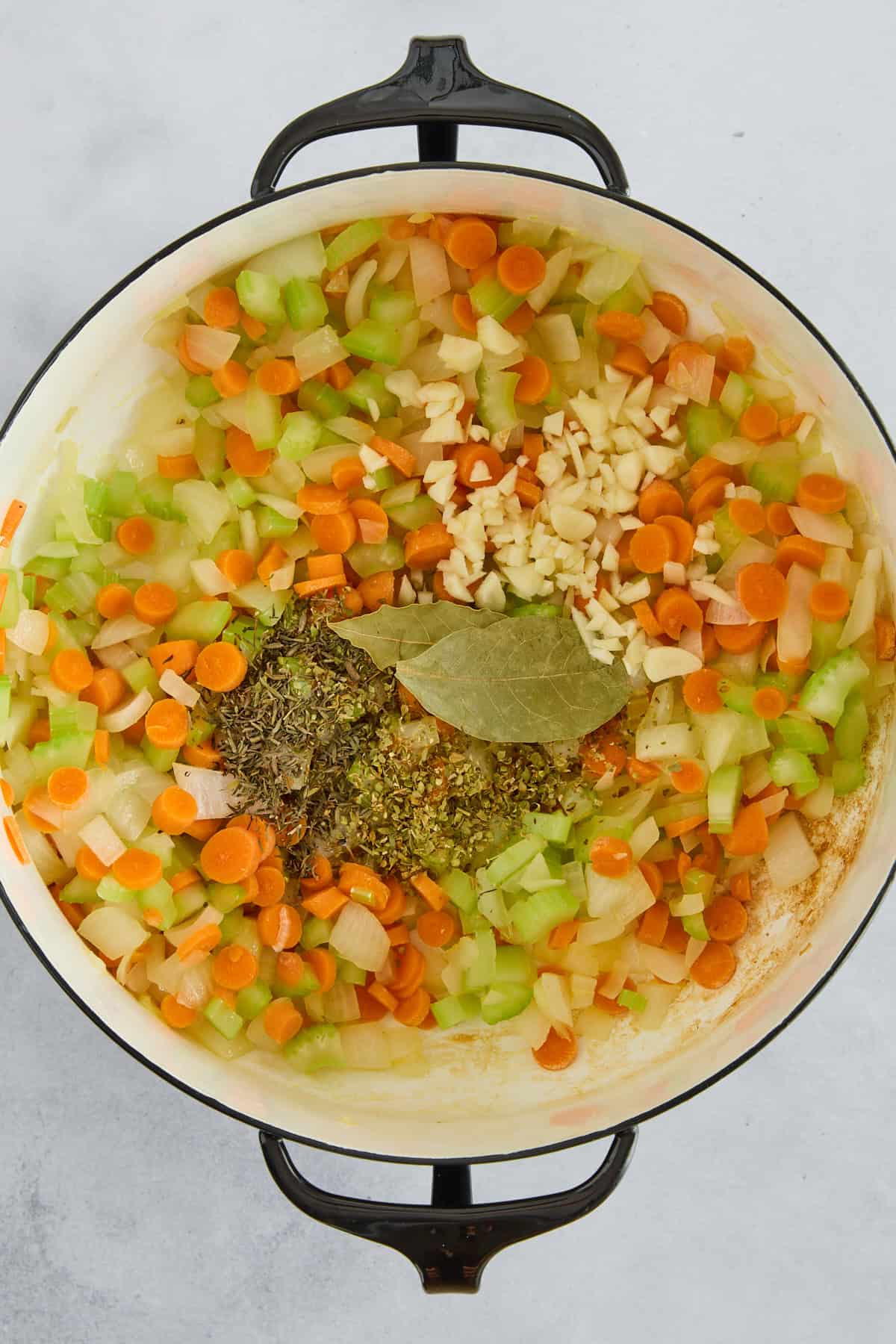 Carrots, onions, celery, garlic, bay leaves, and seasonings in a pot.