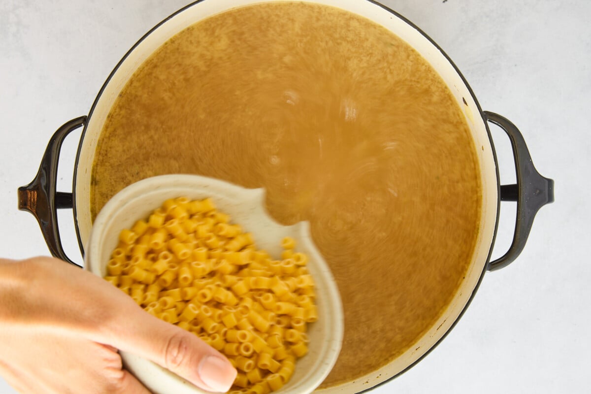 Ditalini pasta being added to a pot of chicken noodle soup.