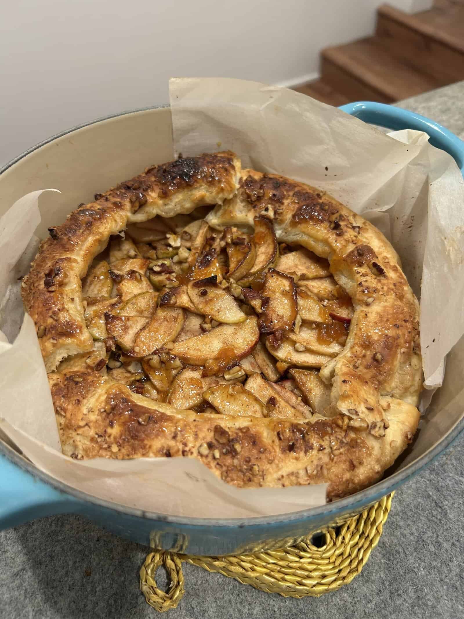 A freshly baked apple galette with a golden, flaky crust and sliced apples inside, set on parchment paper in a blue baking dish on a kitchen counter.