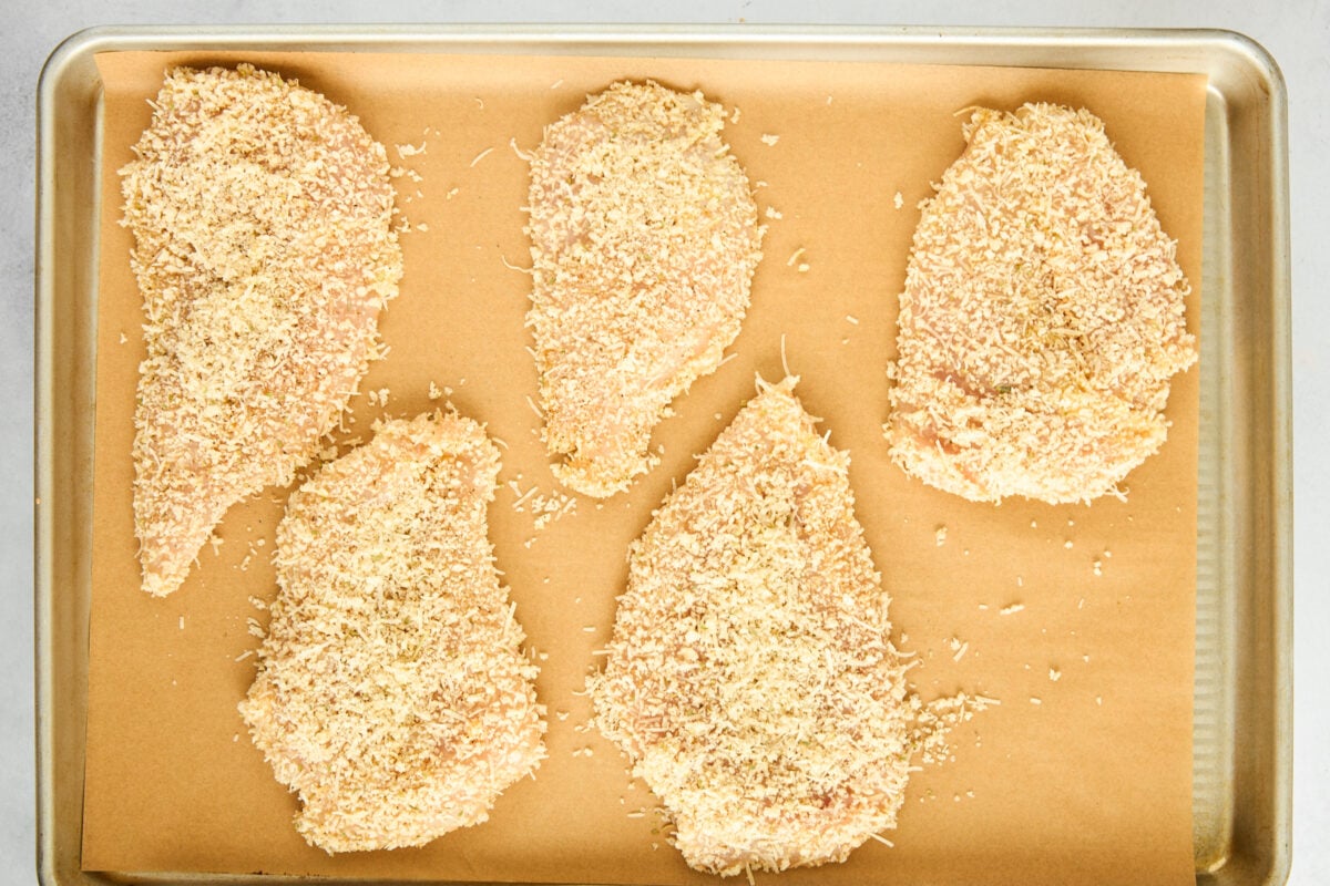 Breaded chicken pieces on a parchment paper lined baking sheet.