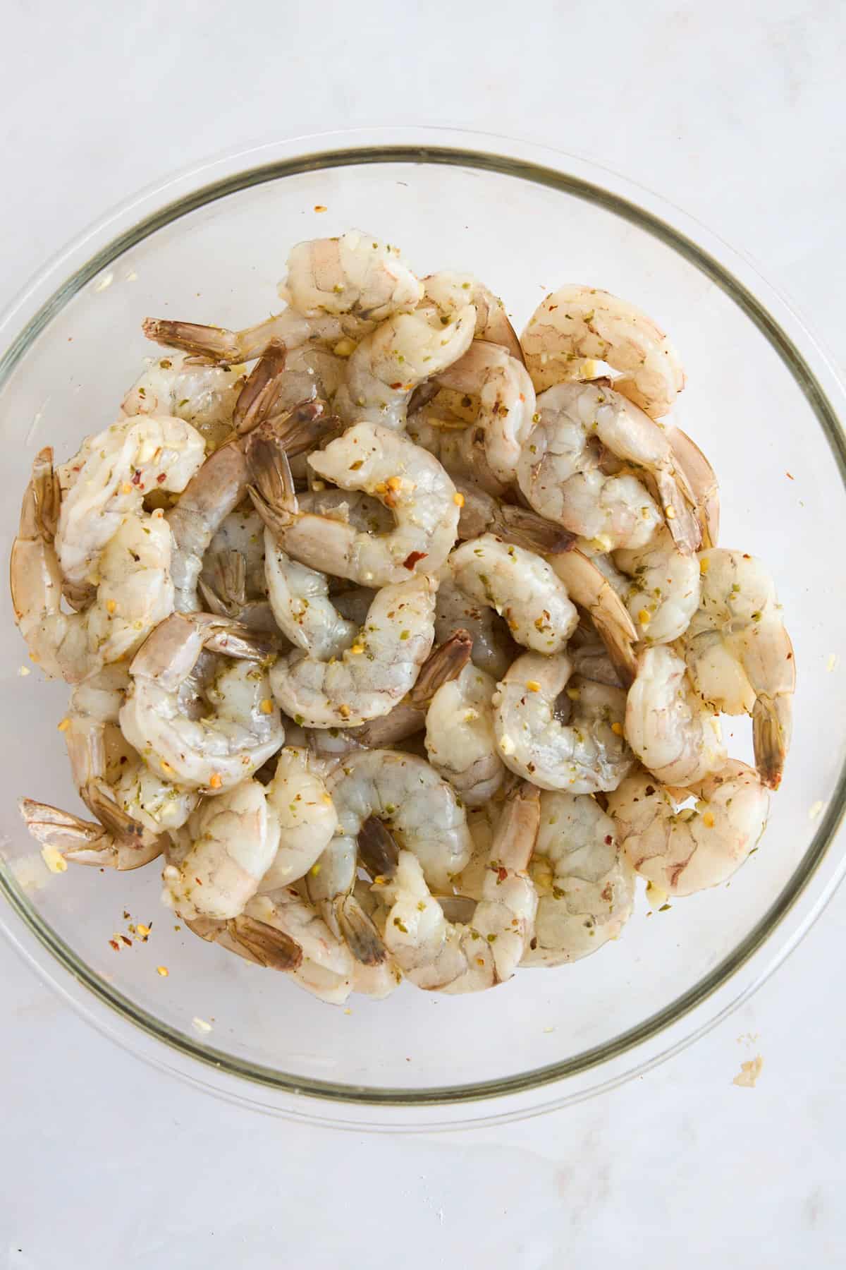 Raw shrimp in a bowl coated with olive oil and seasonings.