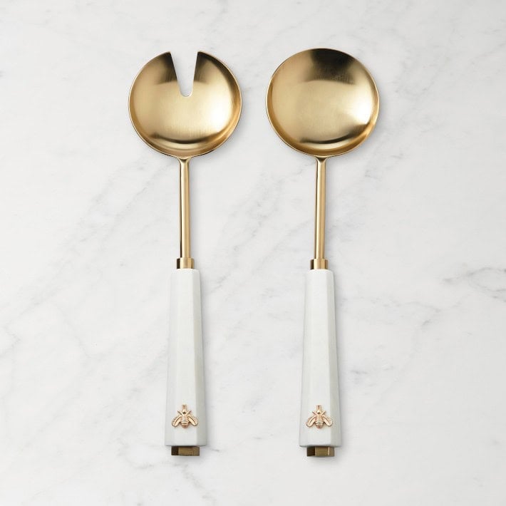A set of two golden salad servers on a marble surface. 
