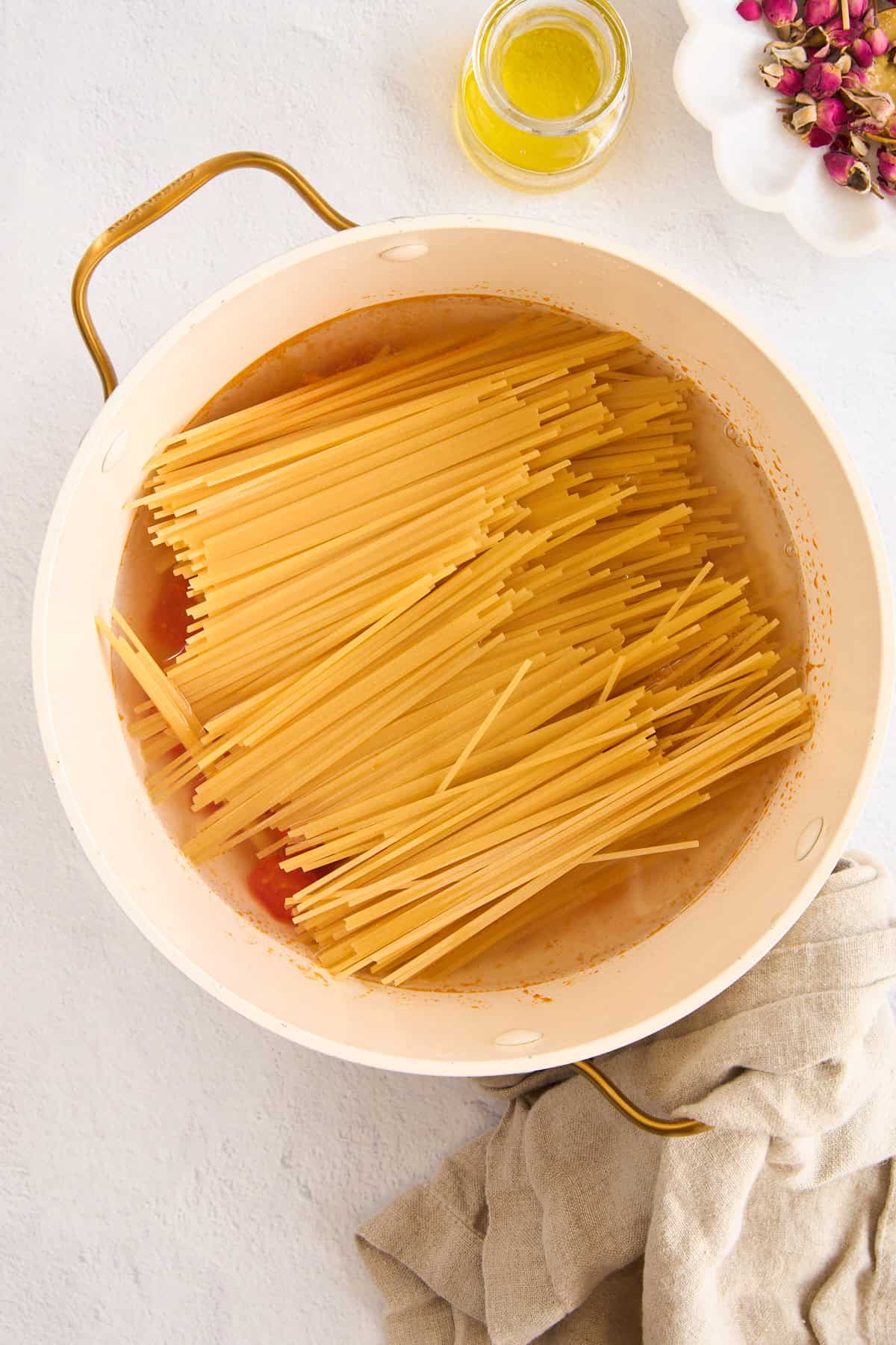 Raw spaghetti on top of tomatoes and garlic in a large pot. 