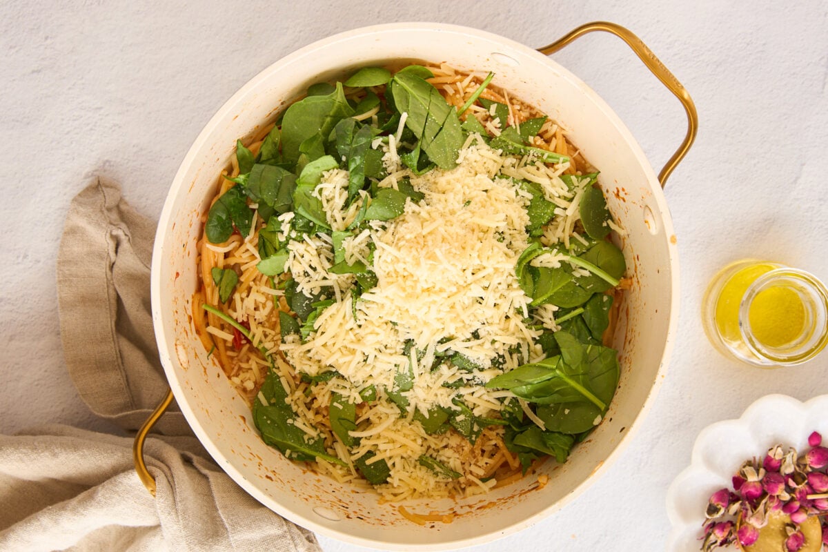 Spinach and parmesan cheese being added to a pot of cooked pasta.