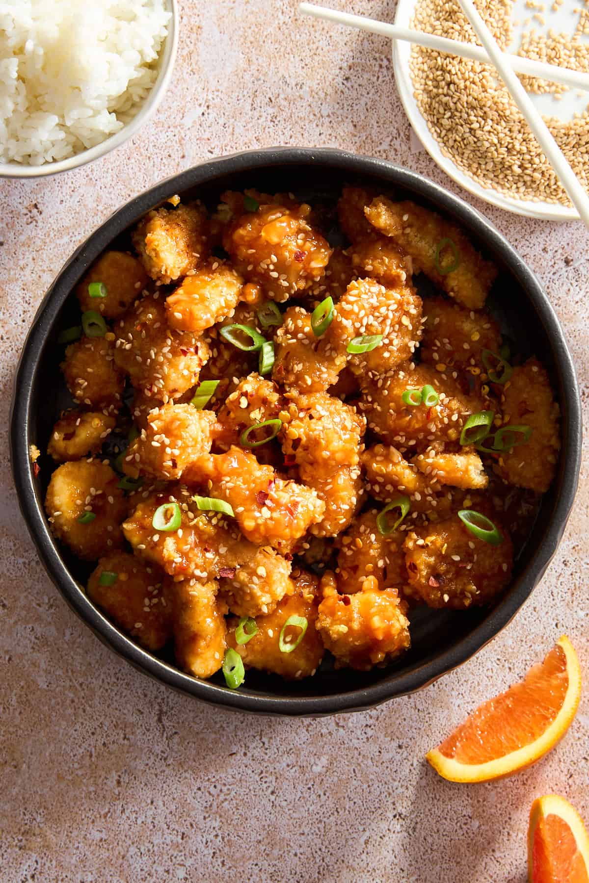 A bowl of orange chicken topped with sesame seeds and green onion.