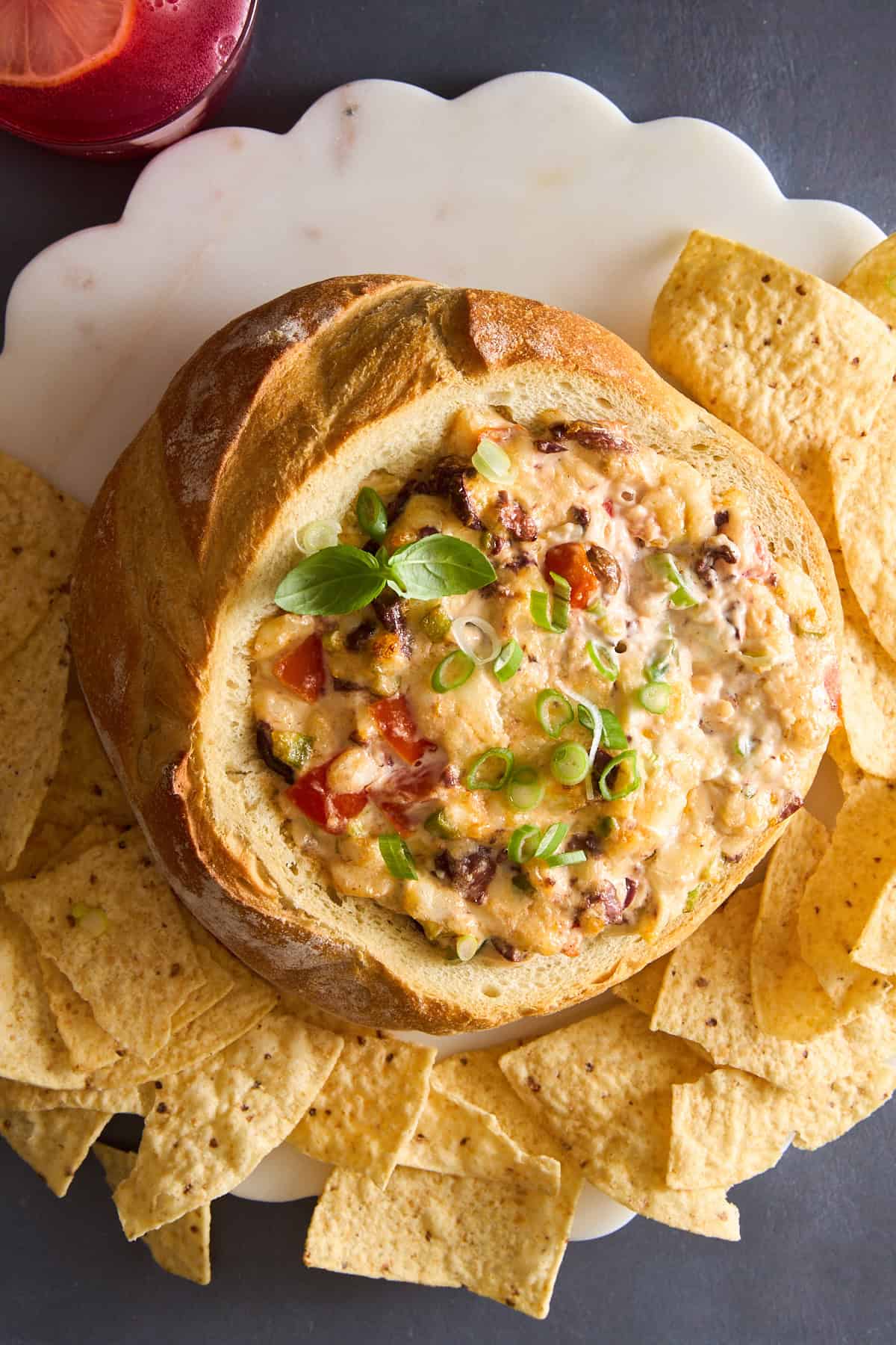 A bread bowl full of cheese dip surrounded by tortilla chips.
