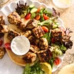 A plate of salad, pita bread, and cooked Mediterranean chicken.