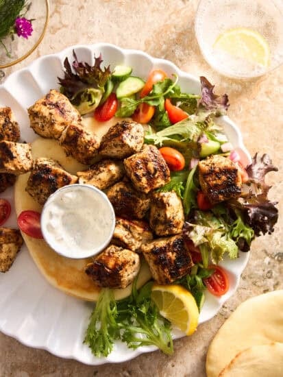 A plate of salad, pita bread, and cooked Mediterranean chicken.