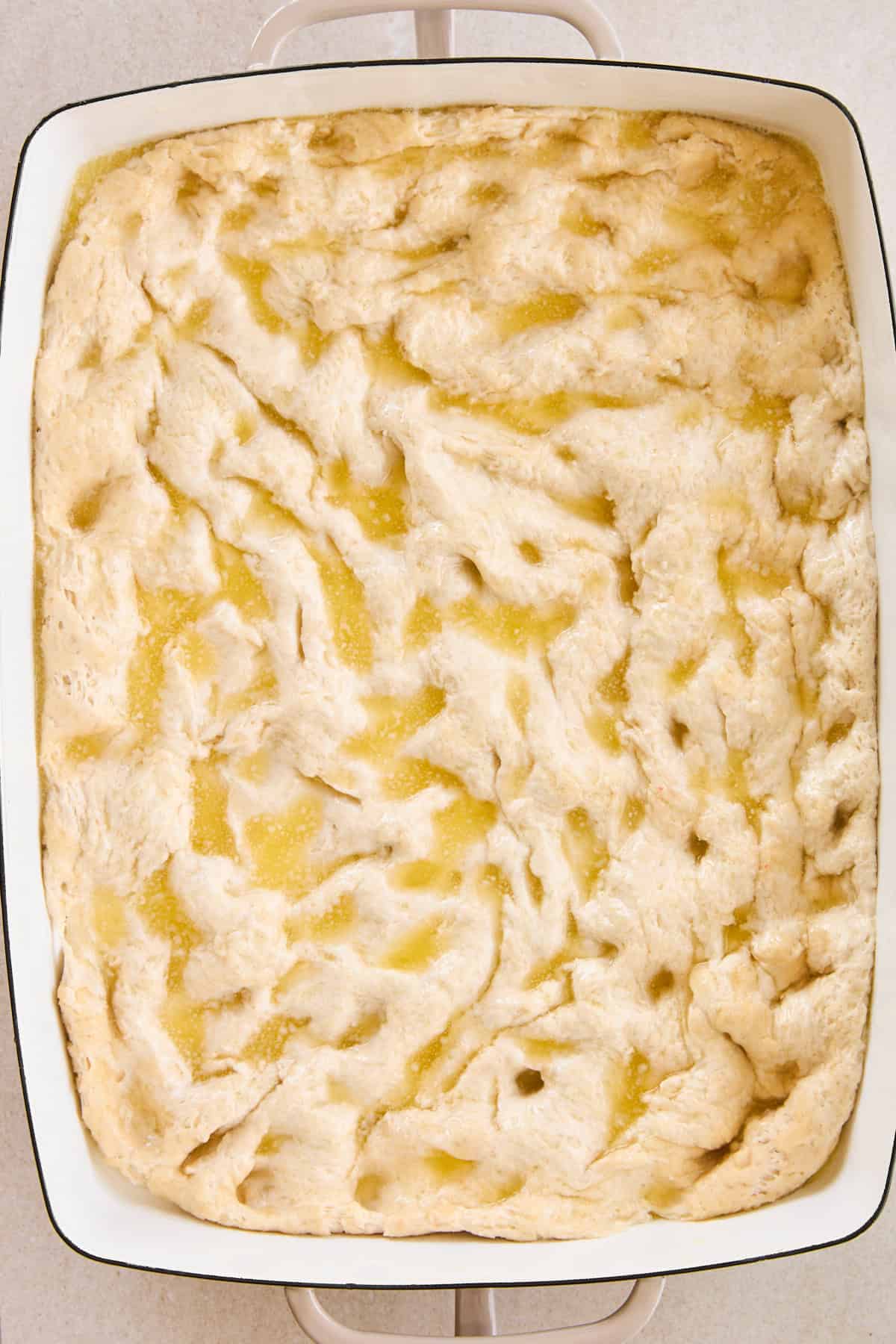 Dimpled focaccia dough in a baking dish topped with olive oil. 