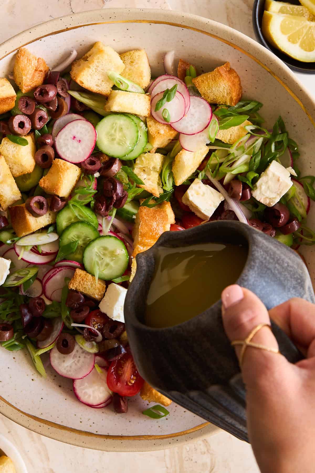 A hand pouring dressing over a bowl of panzanella salad. 