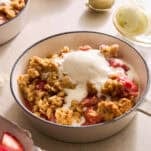 A bowl of strawberry crisp with oat topping topped with a scoop of vanilla ice cream.