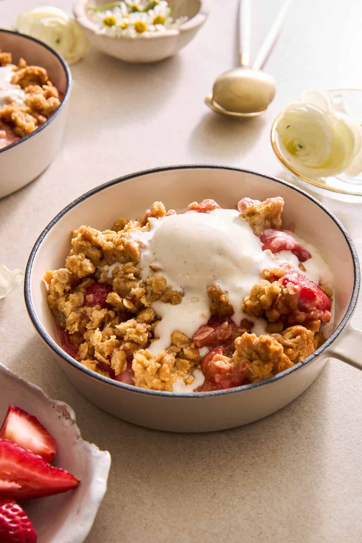 A bowl of strawberry crisp with oat topping topped with a scoop of vanilla ice cream.