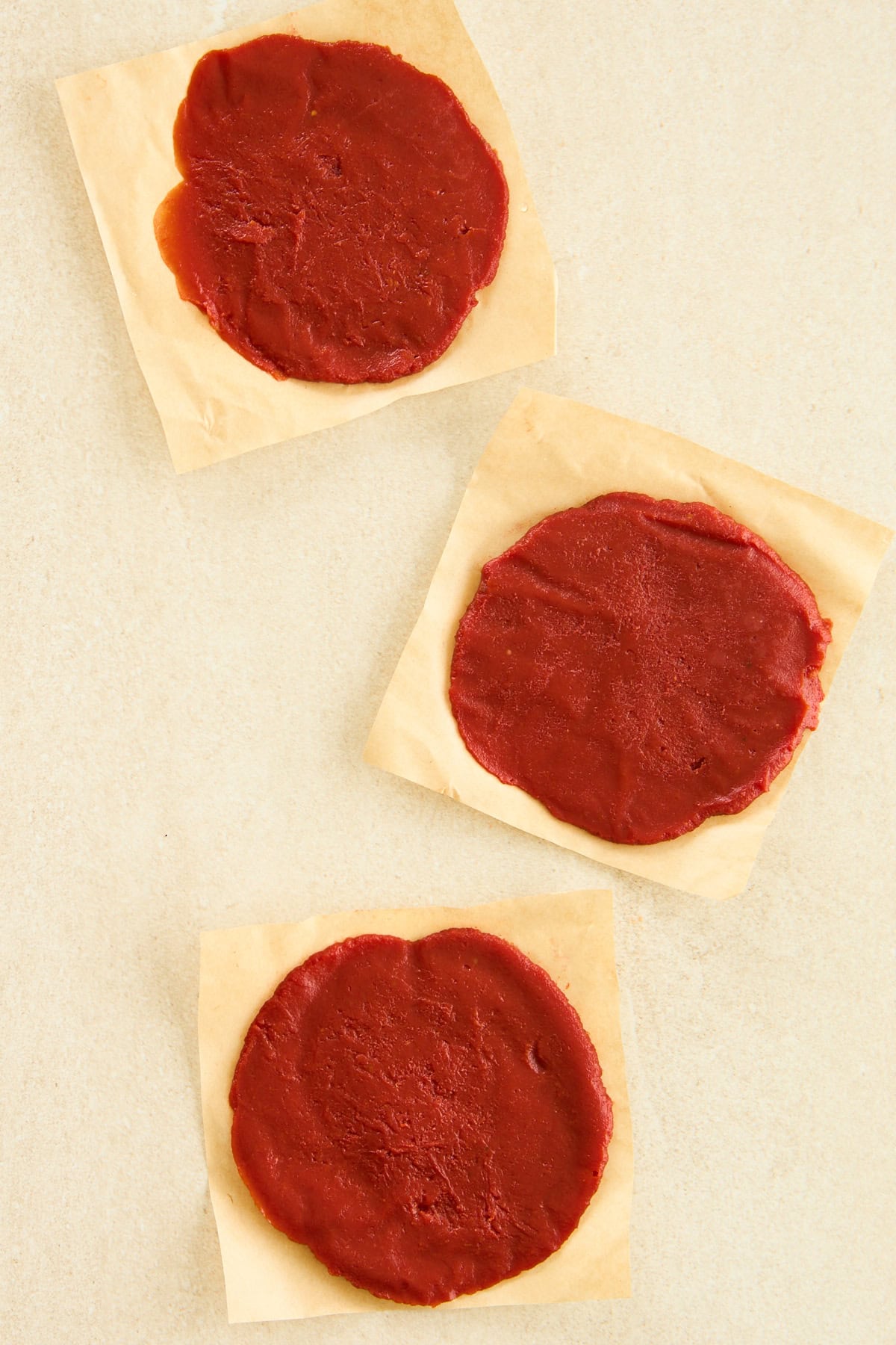 Three frozen tomato paste discs on parchment paper sheets. 