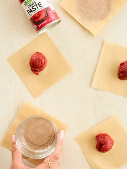 Tomato paste discs being flattened on parchment paper sheets.