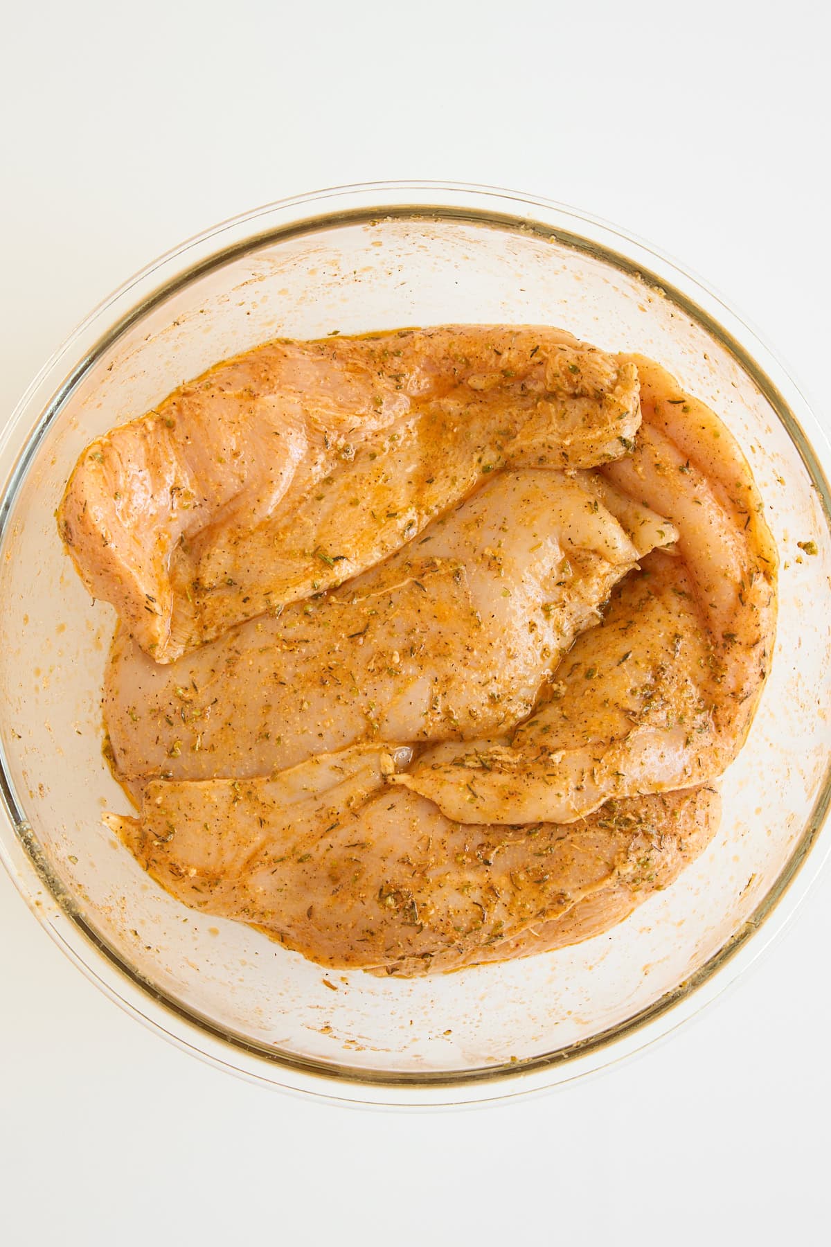Raw chicken breasts marinating in a bowl. 