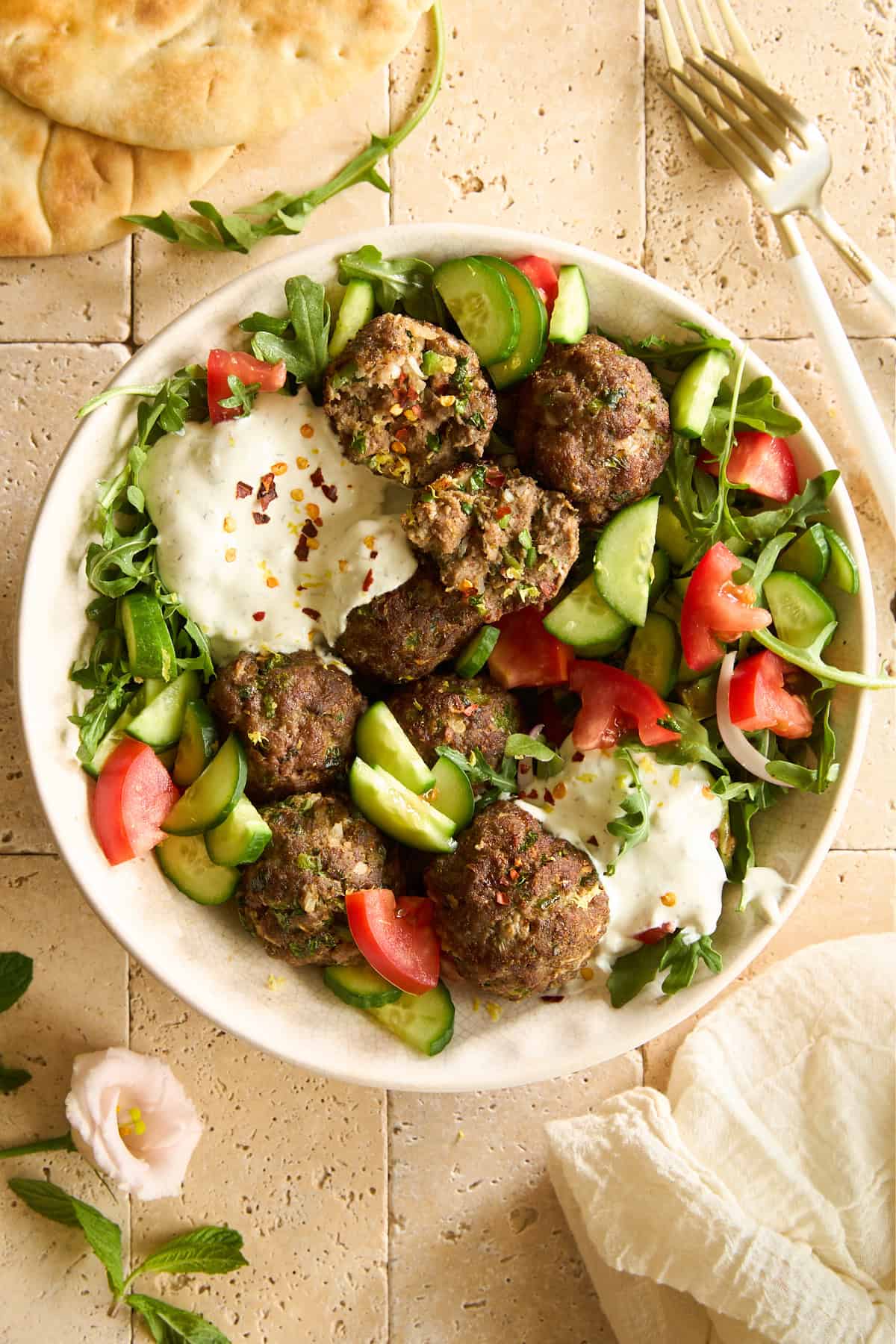A salad with tomatoes, cucumbers, beef kofta meatballs, and tzatziki.
