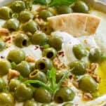 A pita chip sticking out of a bowl of marinated olive dip.