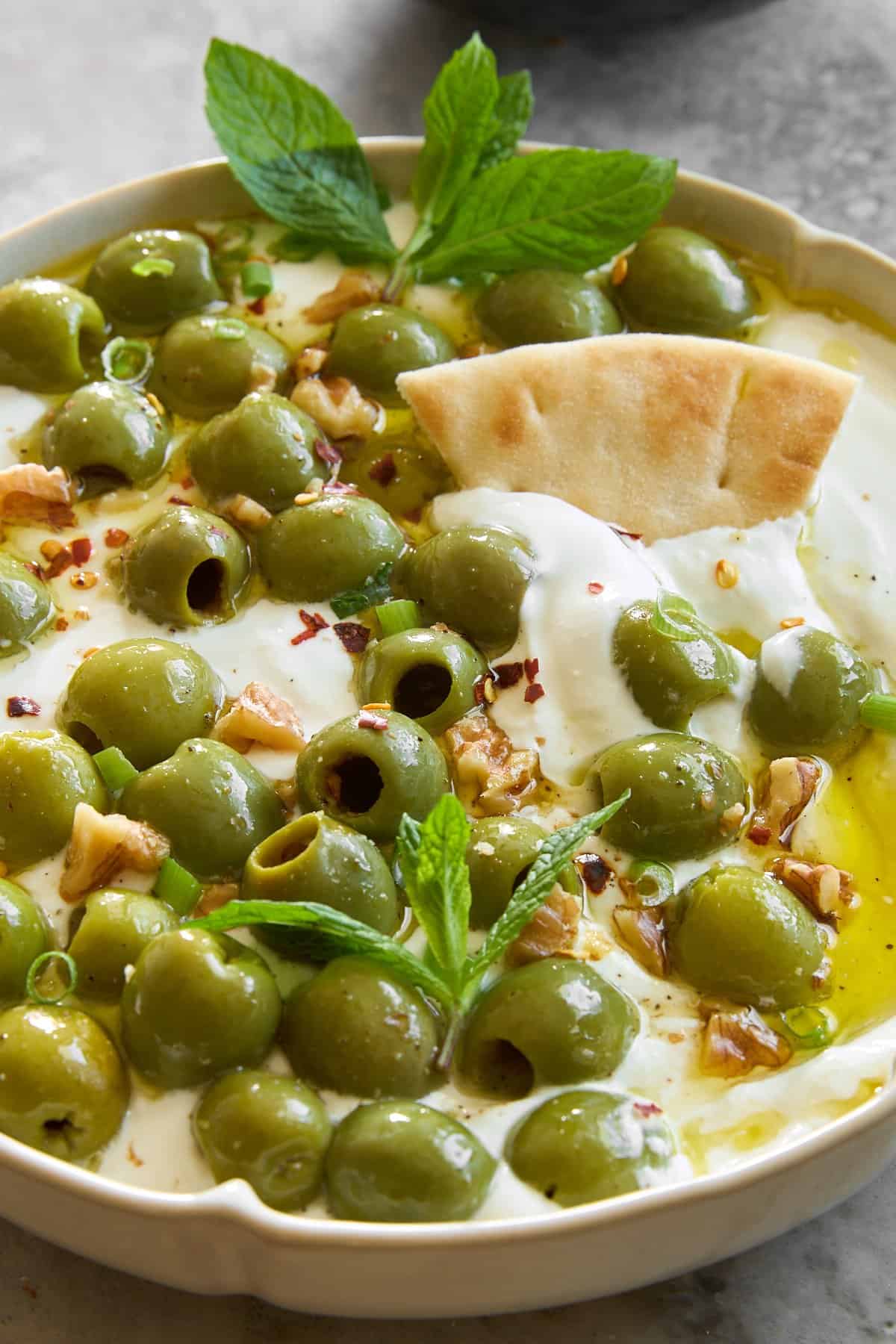 A pita chip sticking out of a bowl of marinated olive dip with whipped cottage cheese. 