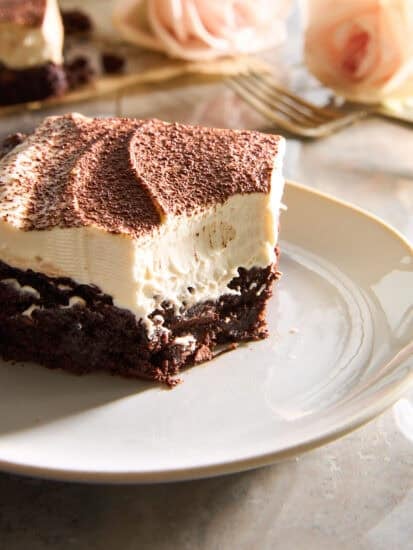 A tiramisu brownie slice on a plate with a corner bite missing.