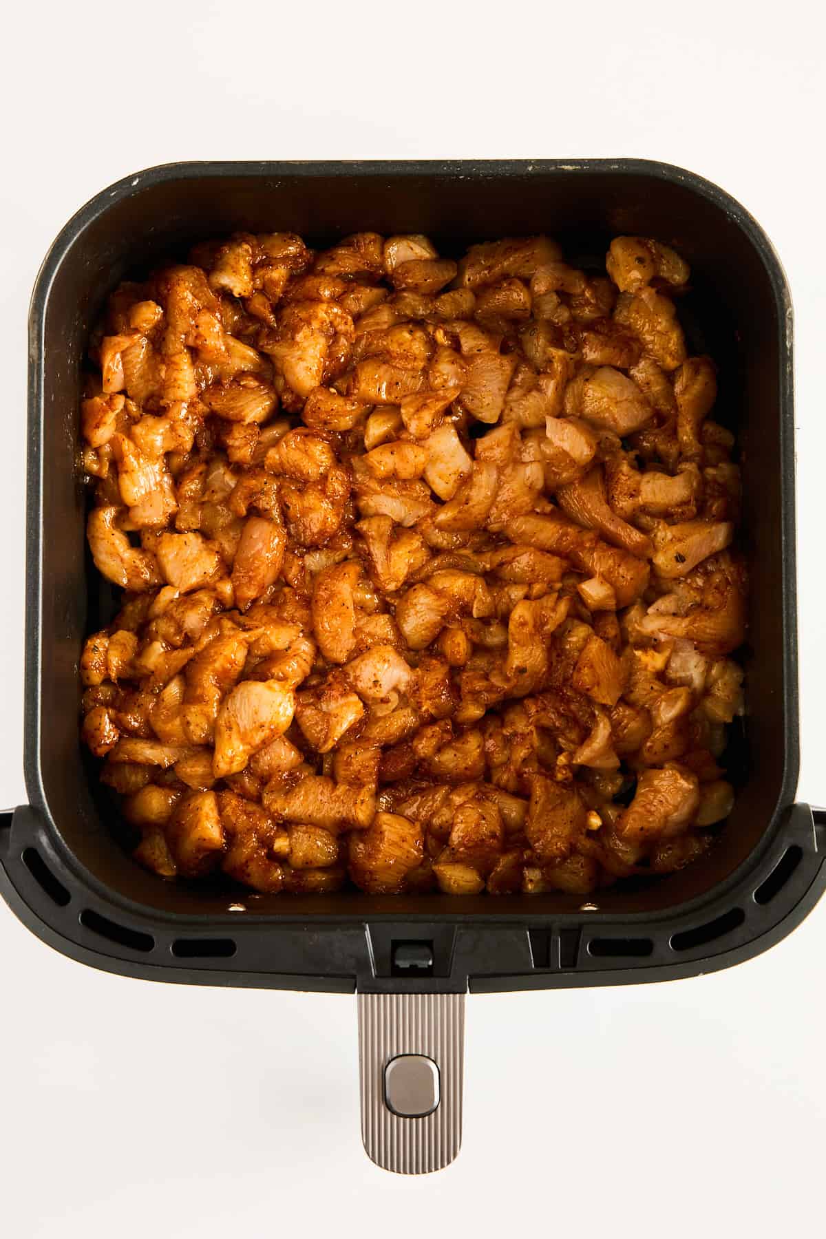 Chunks of marinated, seasoned chicken pieces arranged in the basket of an air fryer, ready to be cooked.