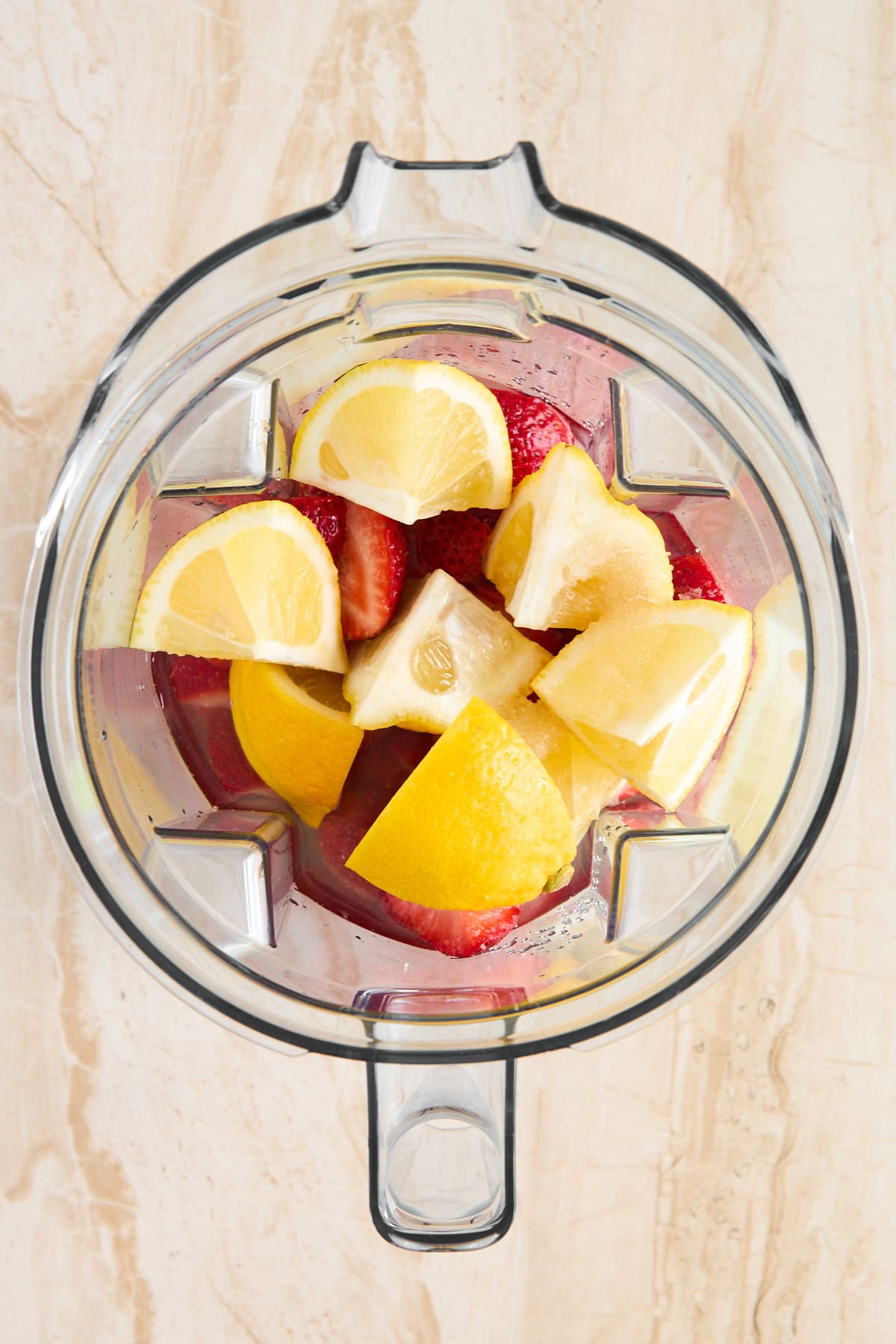 A blender containing lemon and orange wedges along with whole strawberries, ready to be blended.