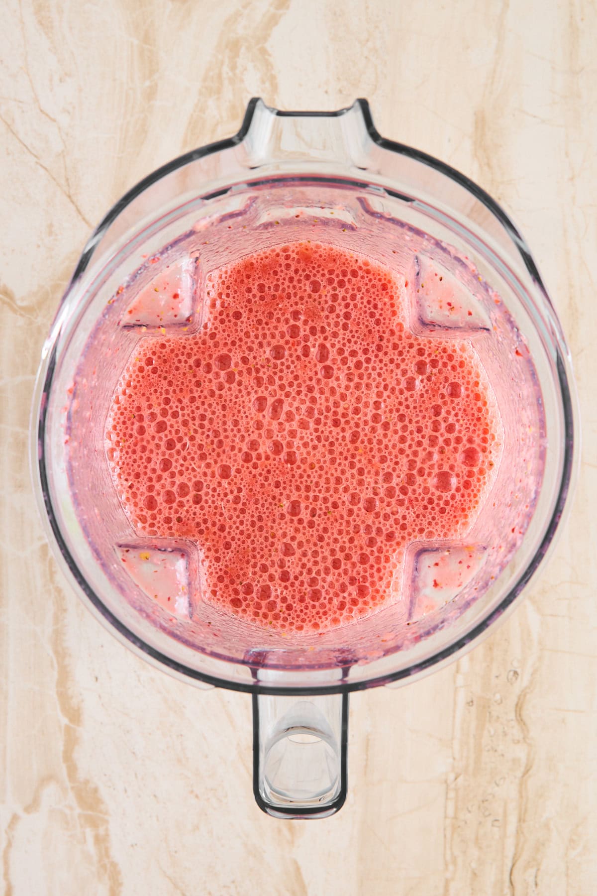 A blender filled with a frothy pink smoothie, sitting on a light-colored, marble-patterned surface.