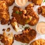 Crispy fried chicken tenders arranged on parchment paper with two ramekins of dipping sauce and a sprinkle of chopped chives.