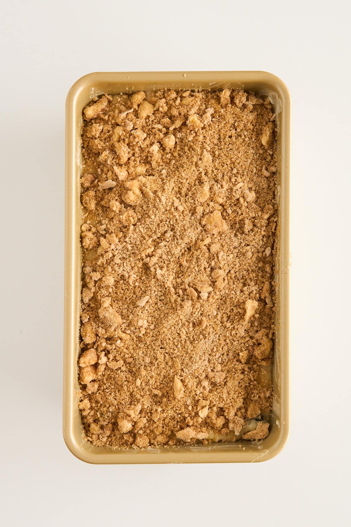 Rectangular baking pan filled with an even layer of crumbly, brown streusel topping on an off-white background.