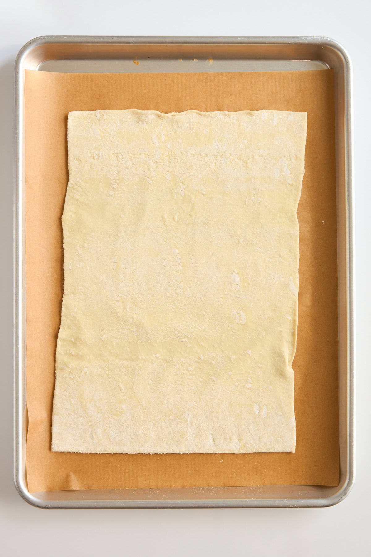 A sheet of uncooked puff pastry is placed on a piece of parchment paper on a baking tray, ready for baking.