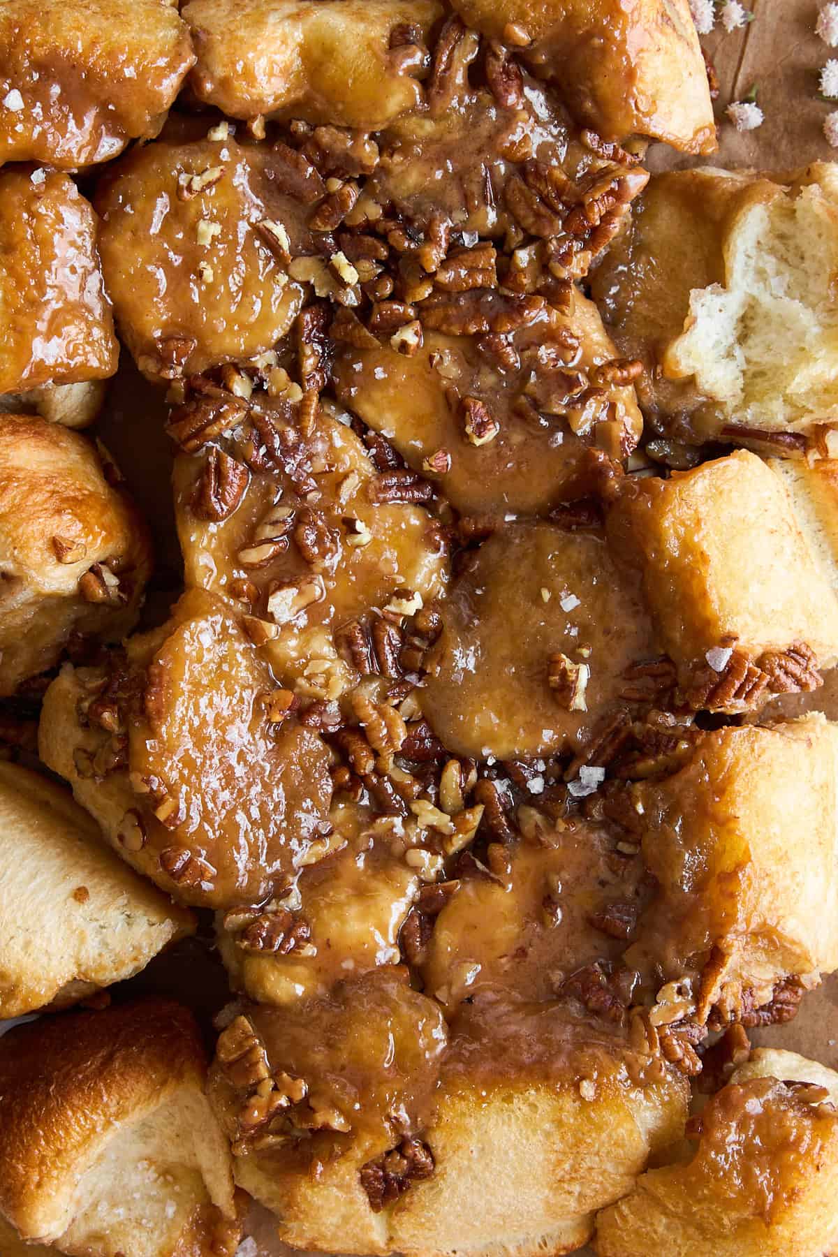 A close-up of sticky, caramel-glazed monkey bread topped with chopped pecans. The bread is golden brown, gooey, and clustered together, with visible pieces of soft, pull-apart dough.