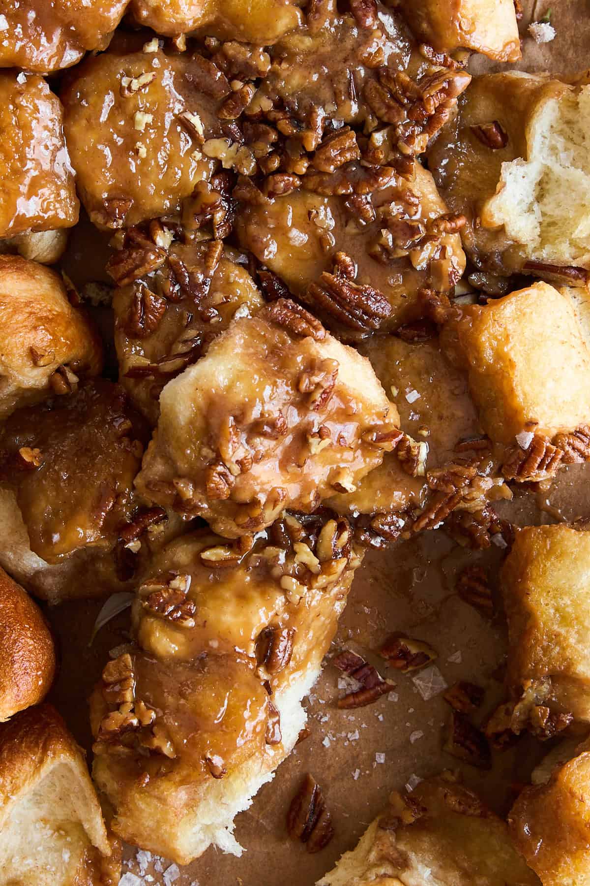 Close-up of golden brown sticky buns topped with caramel sauce and chopped pecans, with pieces pulled apart to reveal their soft, fluffy texture.