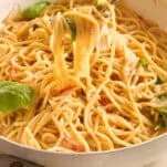 A fork lifts a serving of creamy spaghetti from a white pan, with visible spinach leaves and a light sauce coating the pasta.